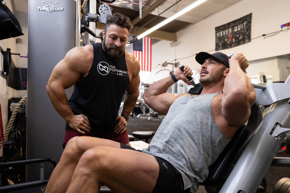 Luke, in a Performance Lab tank, coaching a client through a machine strength exercise