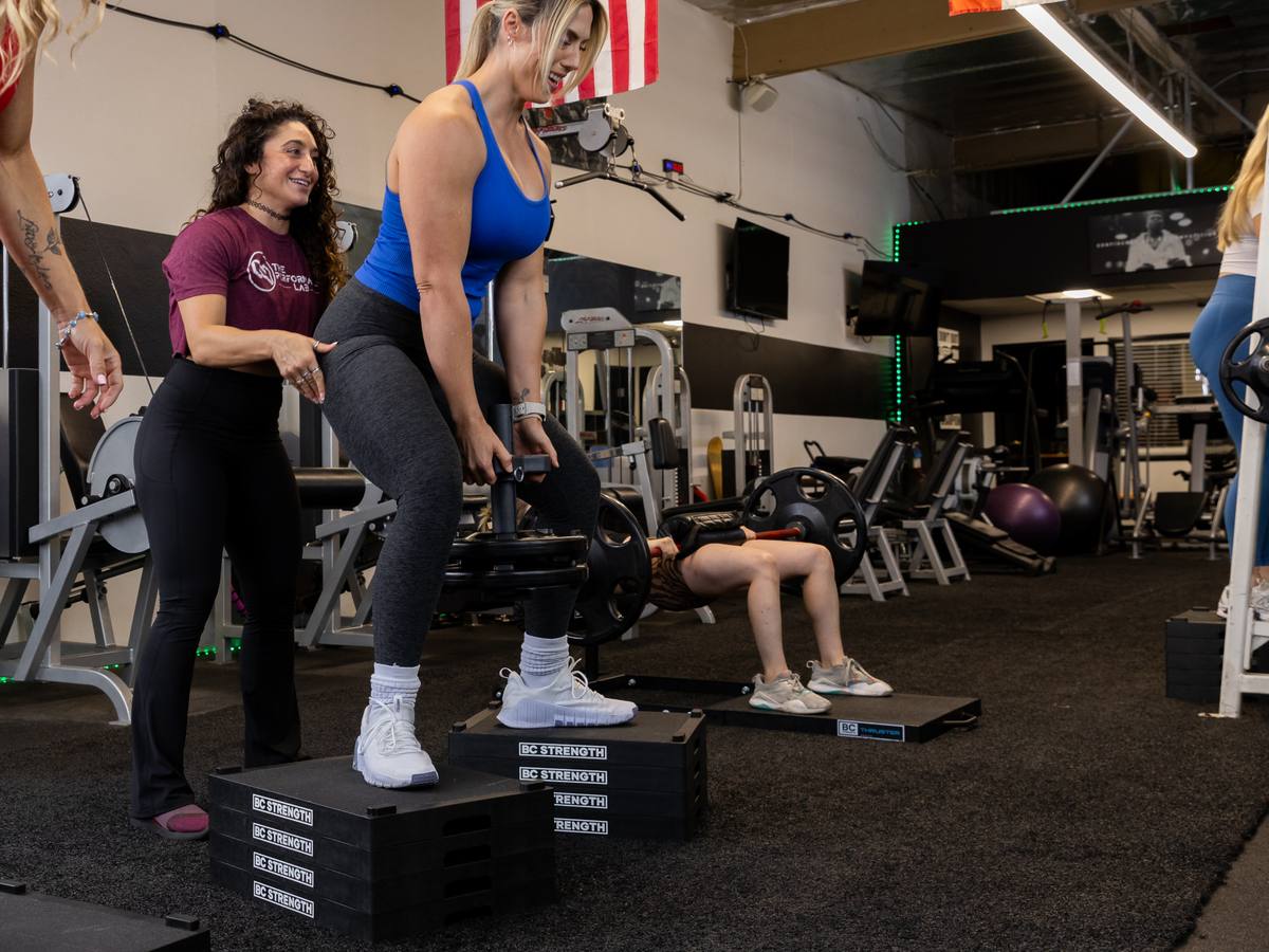 A coach cueing a small group of women through a dumbbell strength station in the studio